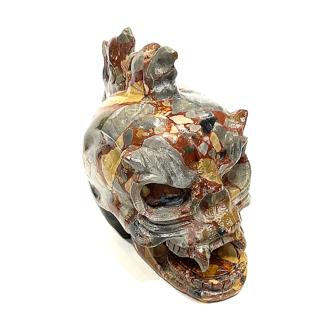 A carved jasper skull alter stones with a dragon mohawk design on a white background, slightly right-angle front view. 