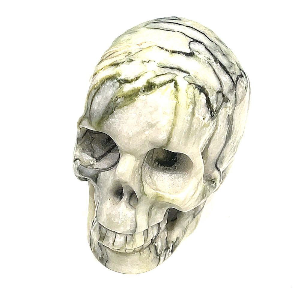 A carved tree-agate skull, white with green throughout, featuring realistic details such as eyes, nose, and mouth, on a white background, front, slight left-angle view. 