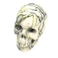 A carved tree-agate skull, white with green throughout, featuring realistic details such as eyes, nose, and mouth, on a white background, front, slight left-angle view. 
