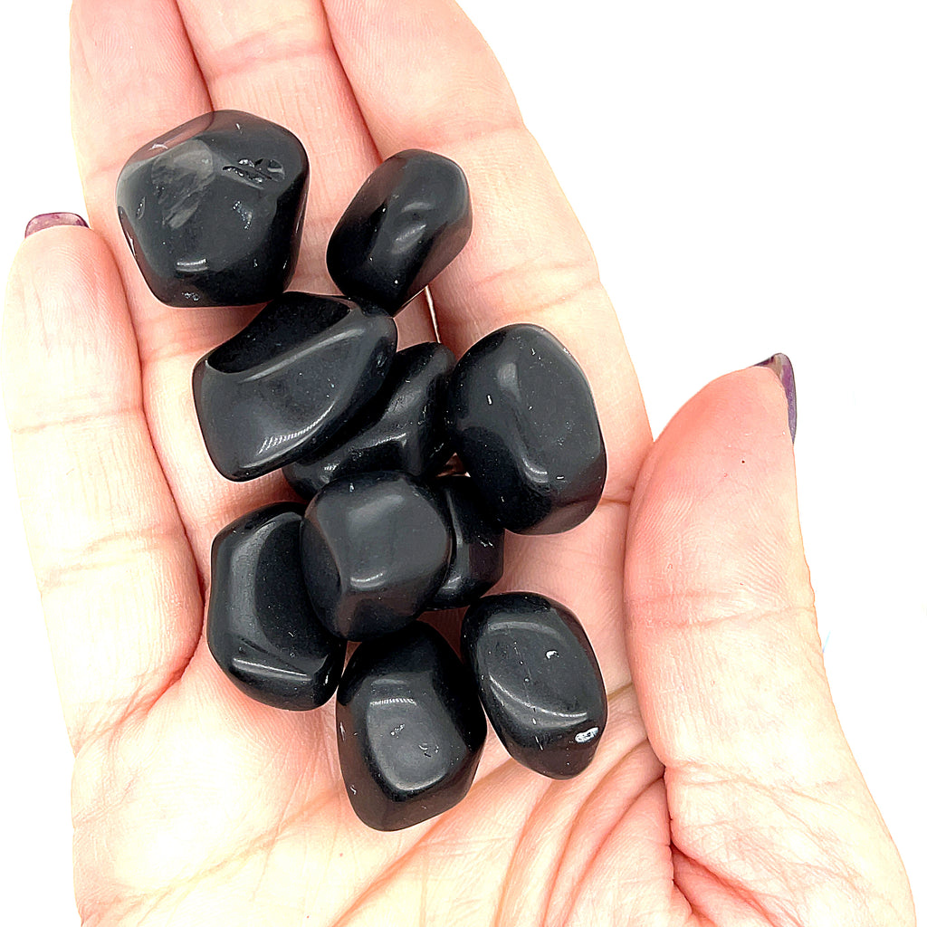 A collection of Apache Tear tumbled gemstones on a white background, in a models hand front overview. 