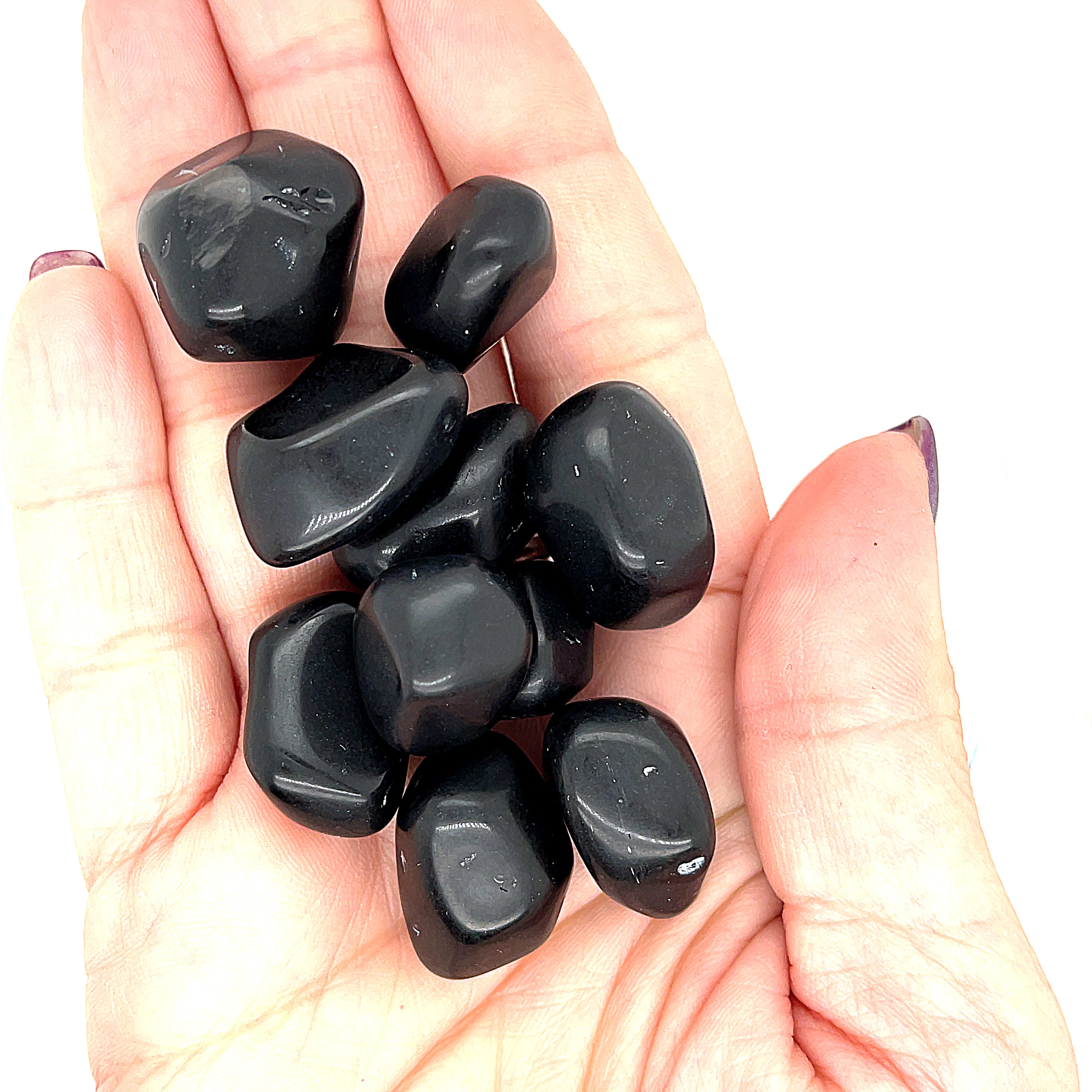 A collection of Apache Tear tumbled gemstones on a white background, in a models hand front overview. 