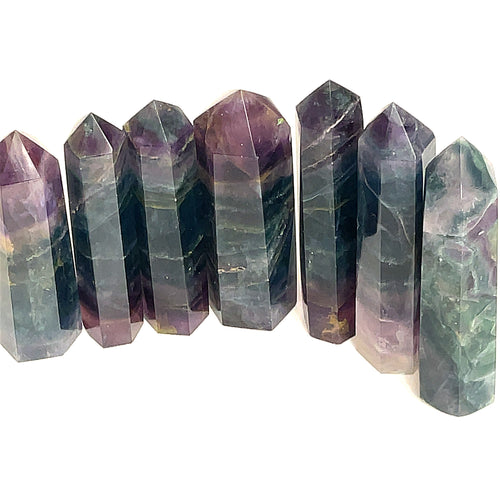 A collection of Blue Fluorite gemstone towers displayed in a row, showing color variations from blue to purple on a white background, front view. 
