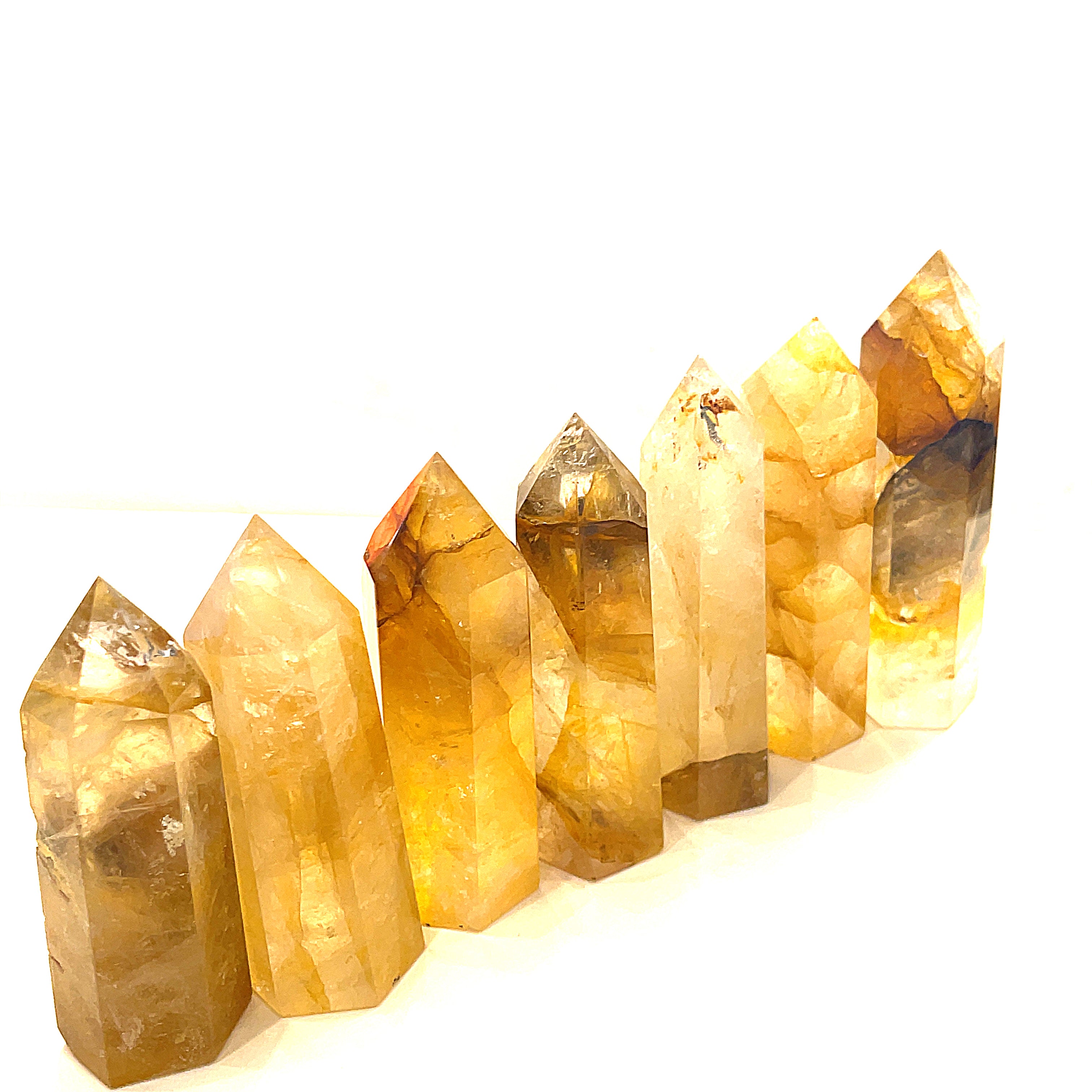A collection of Golden Healer Quartz gemstone towers displayed together in a long line on a white background front close up overview. 