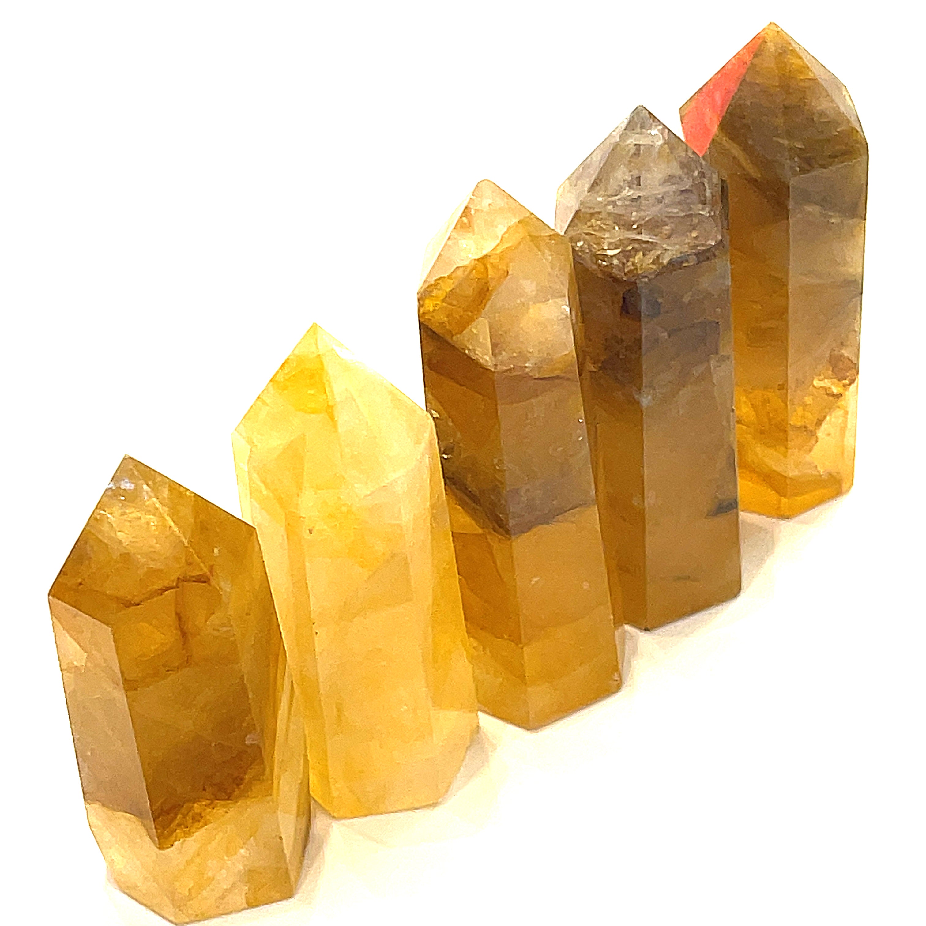 A collection of Golden Healer Quartz gemstone towers displayed together in a long line on a white background front overview. 
