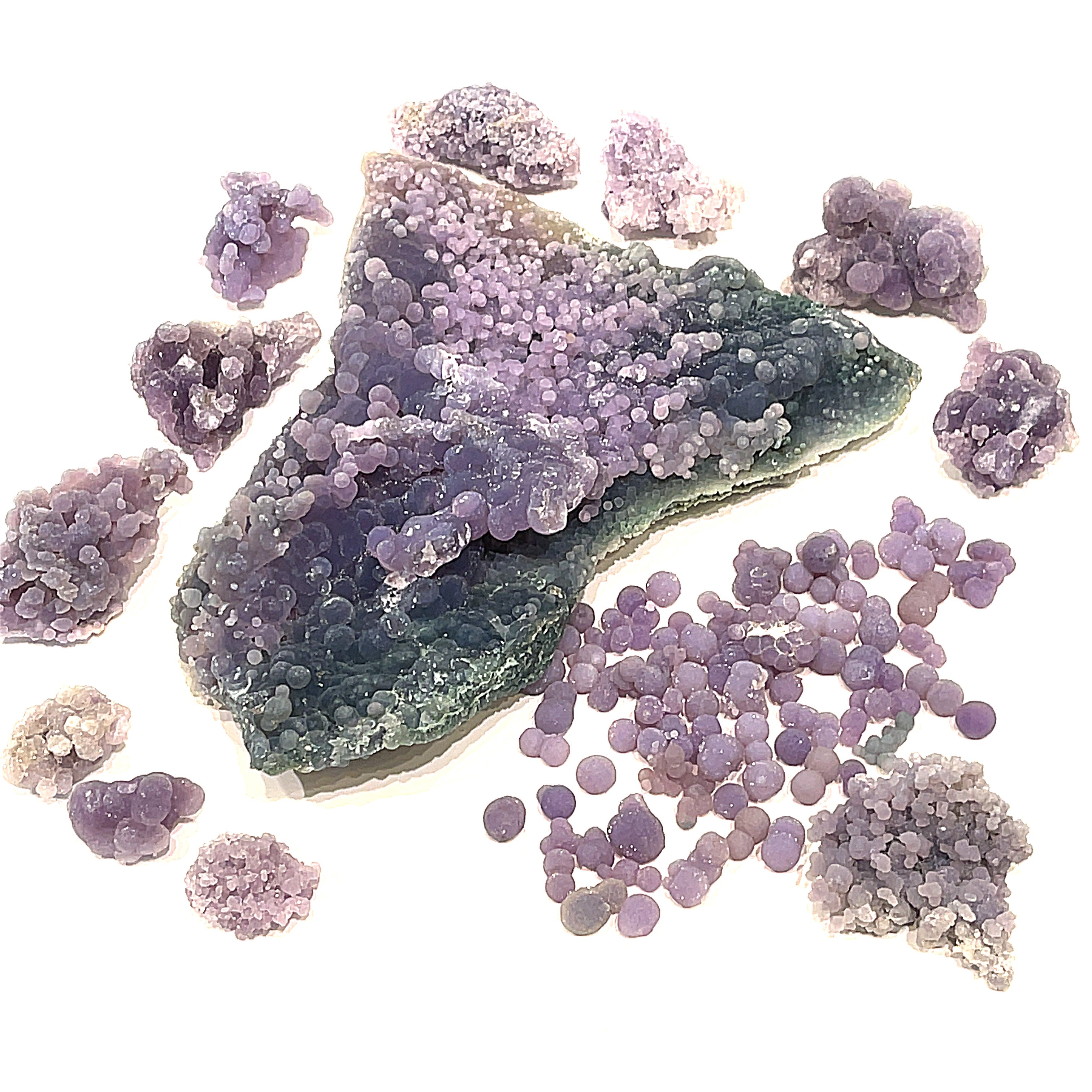 A collection of Grape Agate raw gemstones displayed on a white background, including a variety of shapes and sizes of purple and translucent stones, overview. 