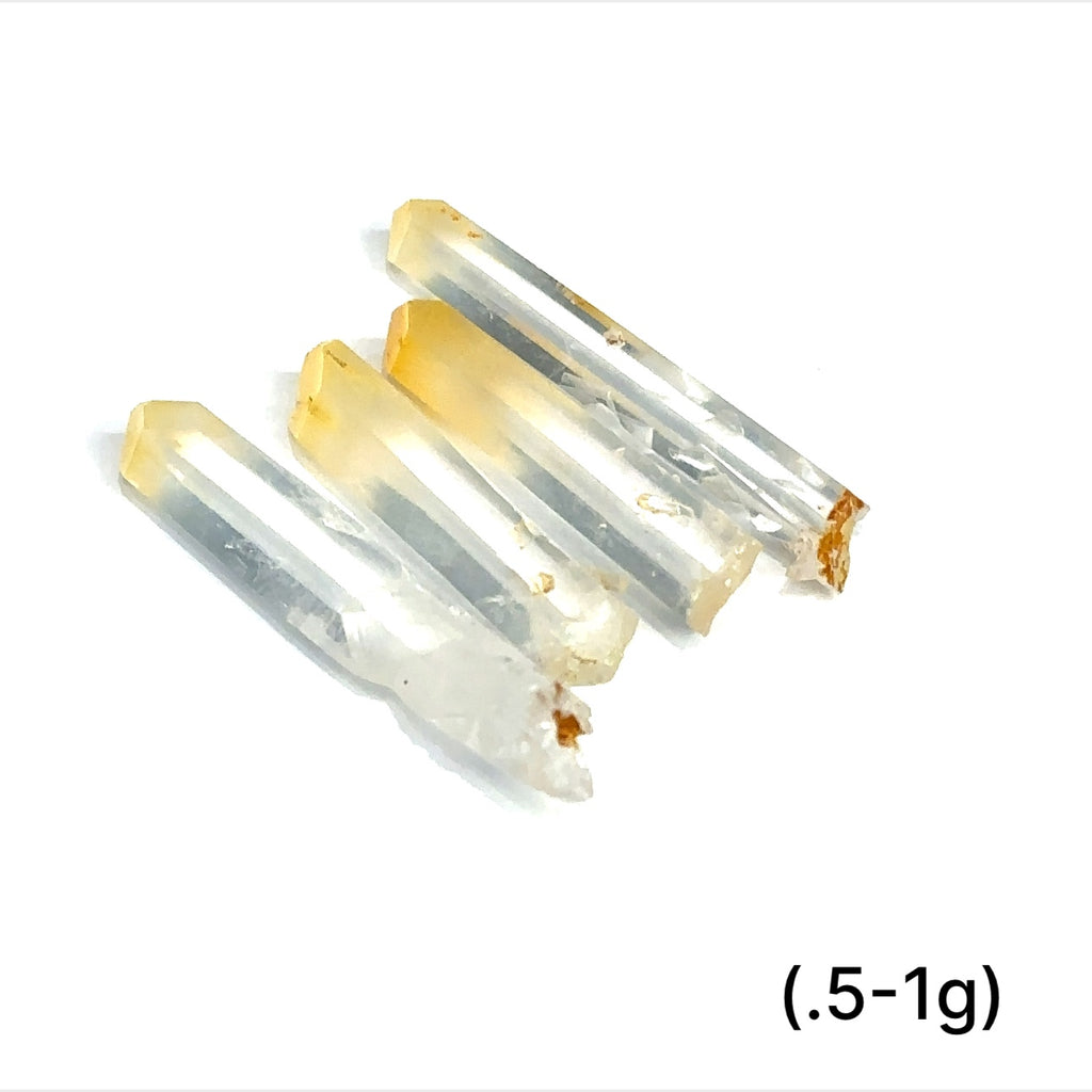 A collection of Halloysite-Included Quartz gemstones, also known as 'Mango Quartz', sizes (.3-1g) is displayed on a white surface center overview.