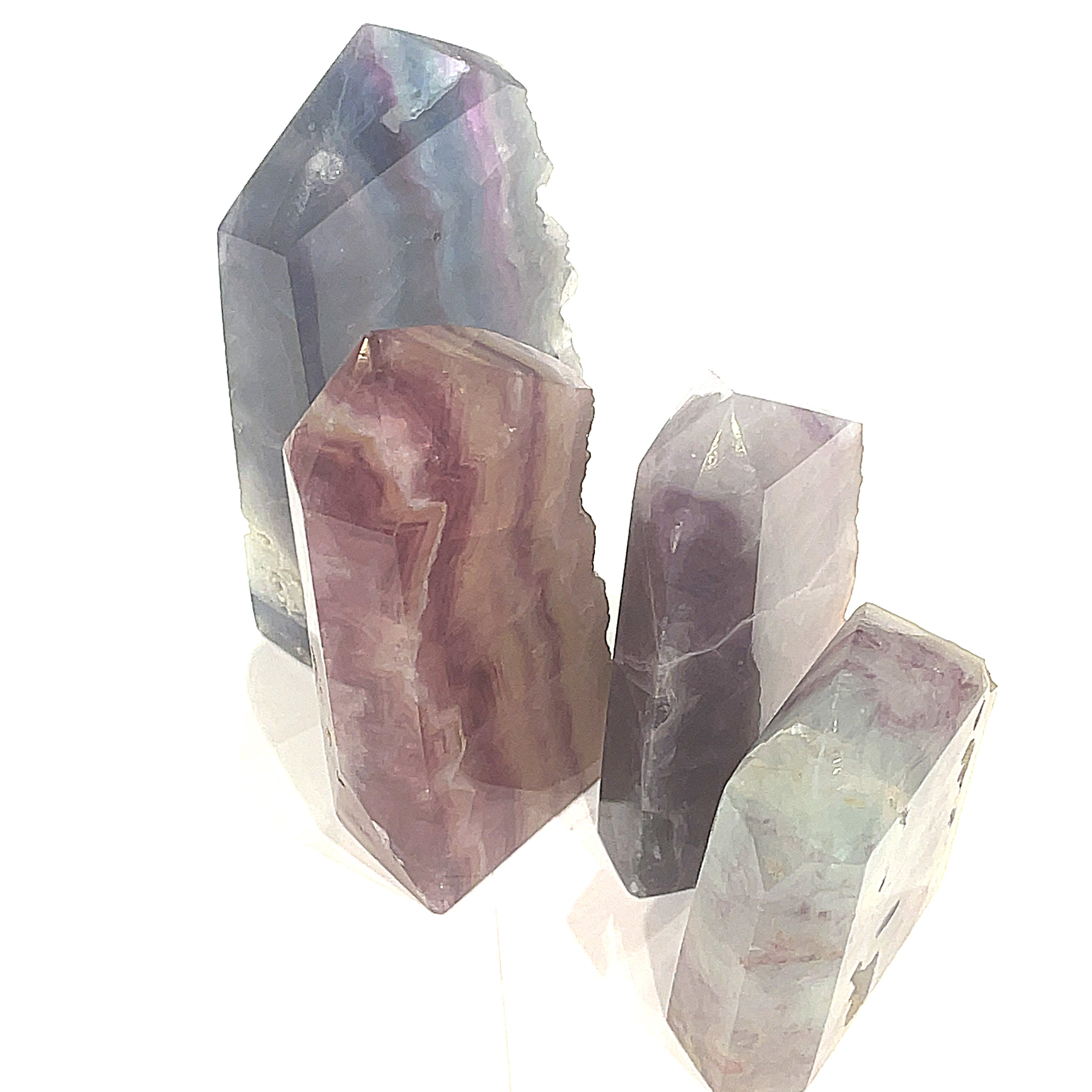 A collection of Rainbow Fluorite Slab gemstone towers in varying sizes, displaying a banding of colors, including purple and blue on a white background, front overview. 