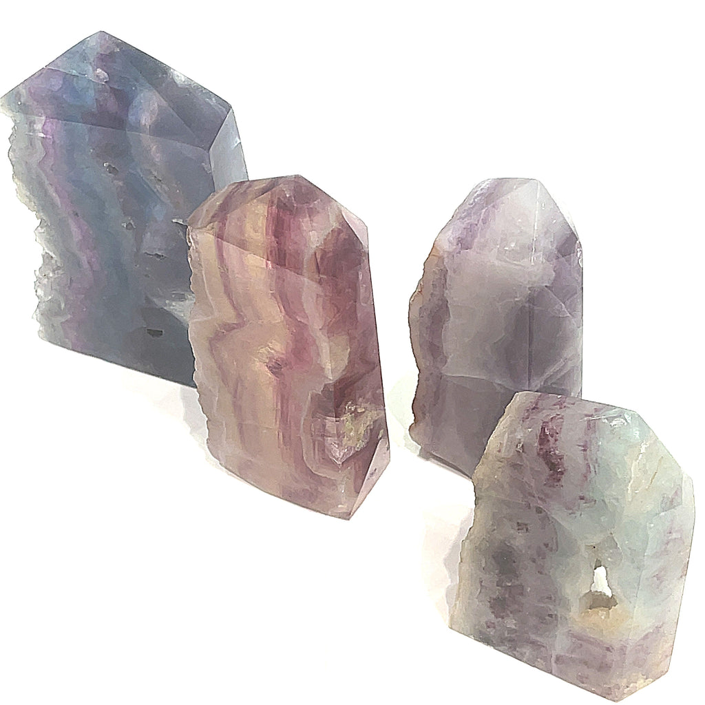 A collection of Rainbow Fluorite Slab gemstone towers in varying sizes, displaying a banding of colors, including purple and blue on a white background, front view. 