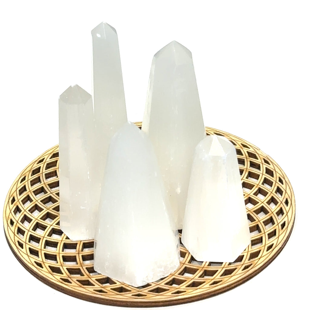 A collection of clear selenite gemstone towers arranged on a circular bamboo tray on a white background, front overview. 