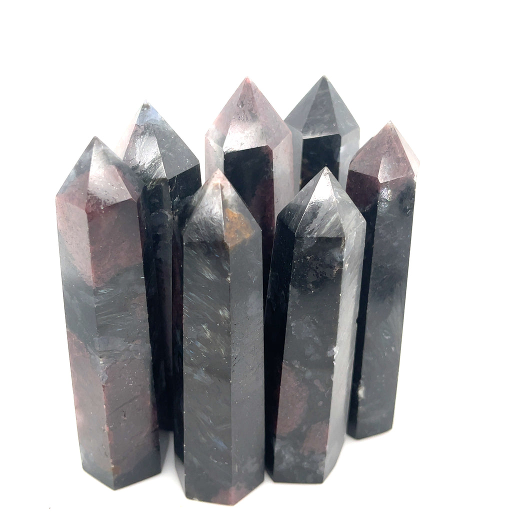 A collection of dark colored gemstone towers arranged in a row, with a variation in size and shape, representing the Garnet and Astrophyllite gemstones on a white background overview. 