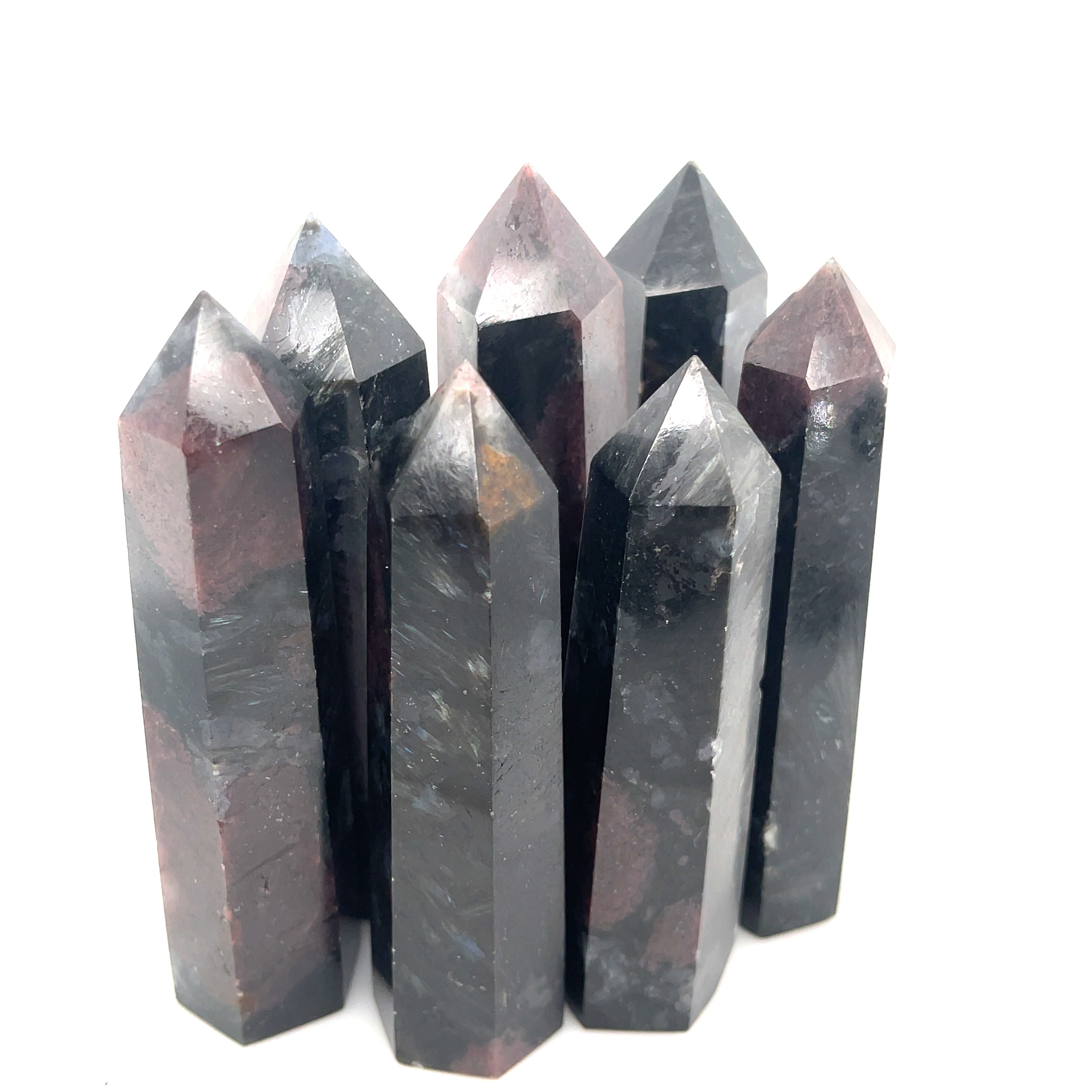 A collection of dark colored gemstone towers arranged in a row, with a variation in size and shape, representing the Garnet and Astrophyllite gemstones on a white background overview. 