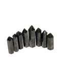 A collection of eight black Arfvedsonite gemstone towers arranged together on a white background, front, close up view. 