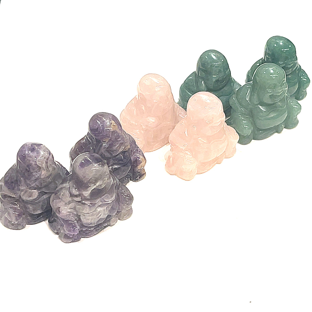 A collection of gemstone carvings in the shape of a Buddha, displayed in a row, with varying colors such as purple, green, and pink on a white background, front view.