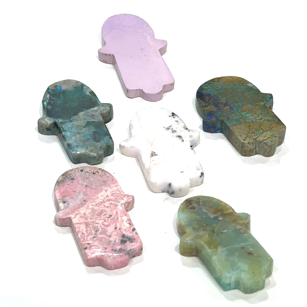 A collection of gemstone carvings in various colors, resembling the Humza shape, is displayed on a white background front overview