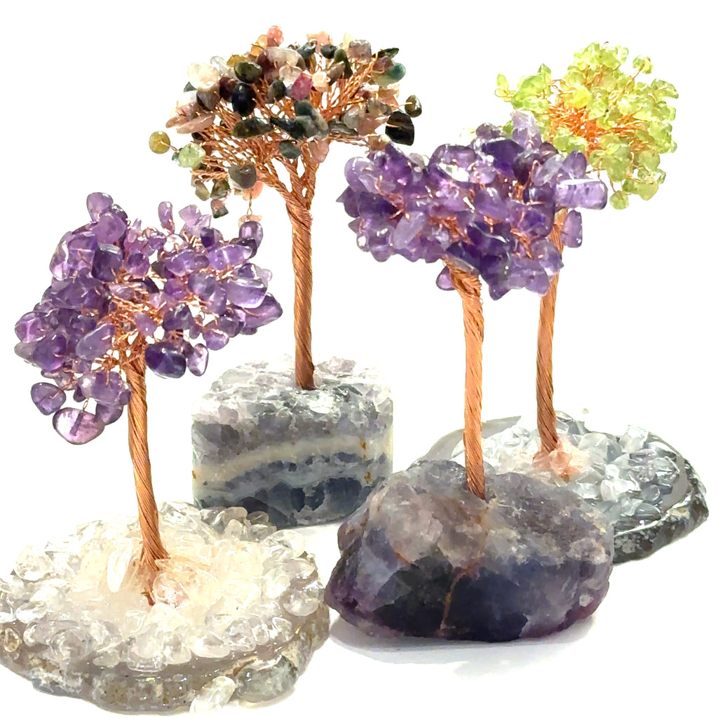 A collection of handcrafted gemstone trees with copper wiring as branches, sitting on natural stone bases with varying colors. On a white background, front view.