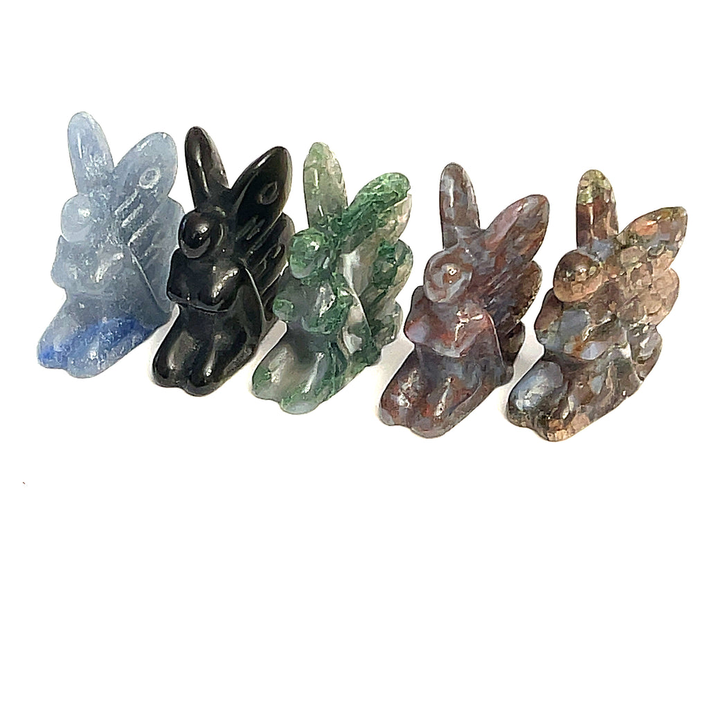 A collection of miniature gemstone carvings in various colors, each resembling a fairy sitting with their hands on their lap, displayed on a white background, front view. 