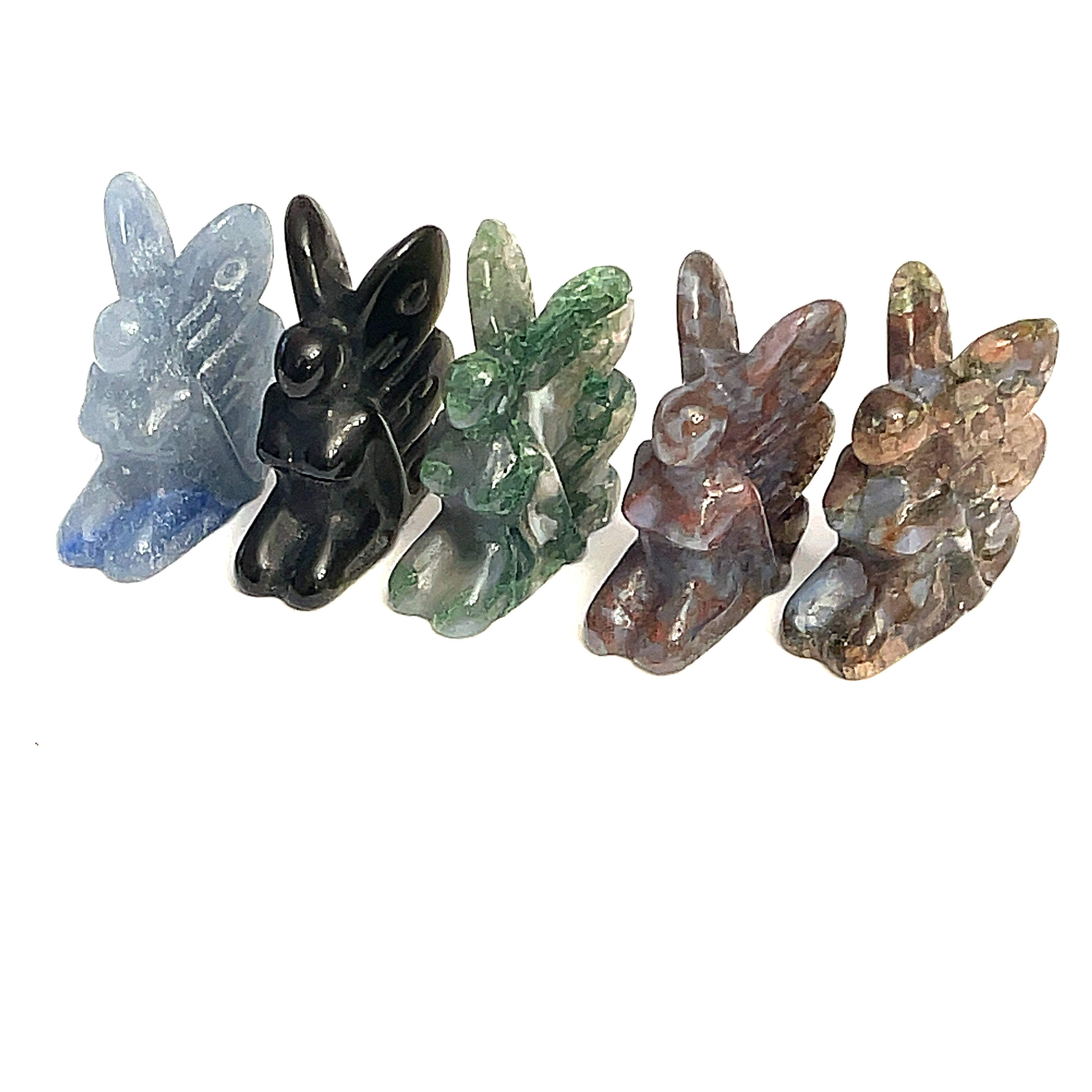 A collection of miniature gemstone carvings in various colors, each resembling a fairy sitting with their hands on their lap, displayed on a white background, front view. 