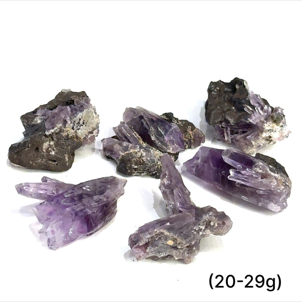 A collection of raw Guerrero Amethyst gemstones with varying crystal structures, predominantly in purple color, against a white background, with sizes ranging from 20 to 29g, front overview