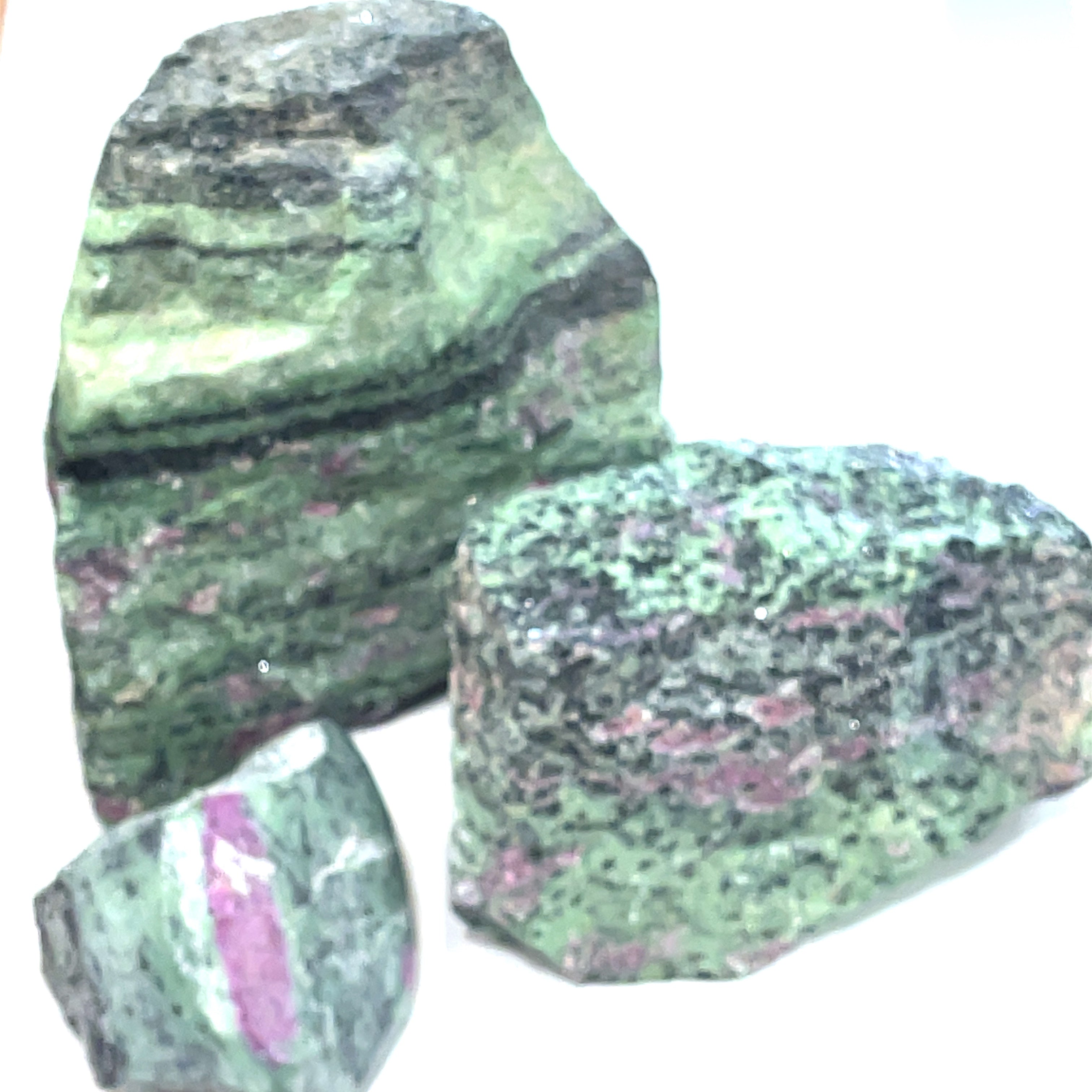 A collection of raw Ruby in Zoisite gemstones with a greenish tinge and visible pink inclusions on a white background, front view.