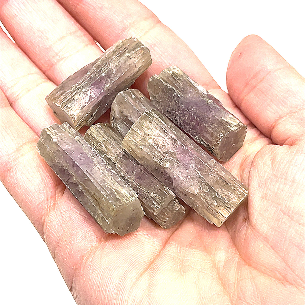 A collection of raw Spanish (Purple) Aragonite gemstones displayed in a models palm on a white background, front overview.