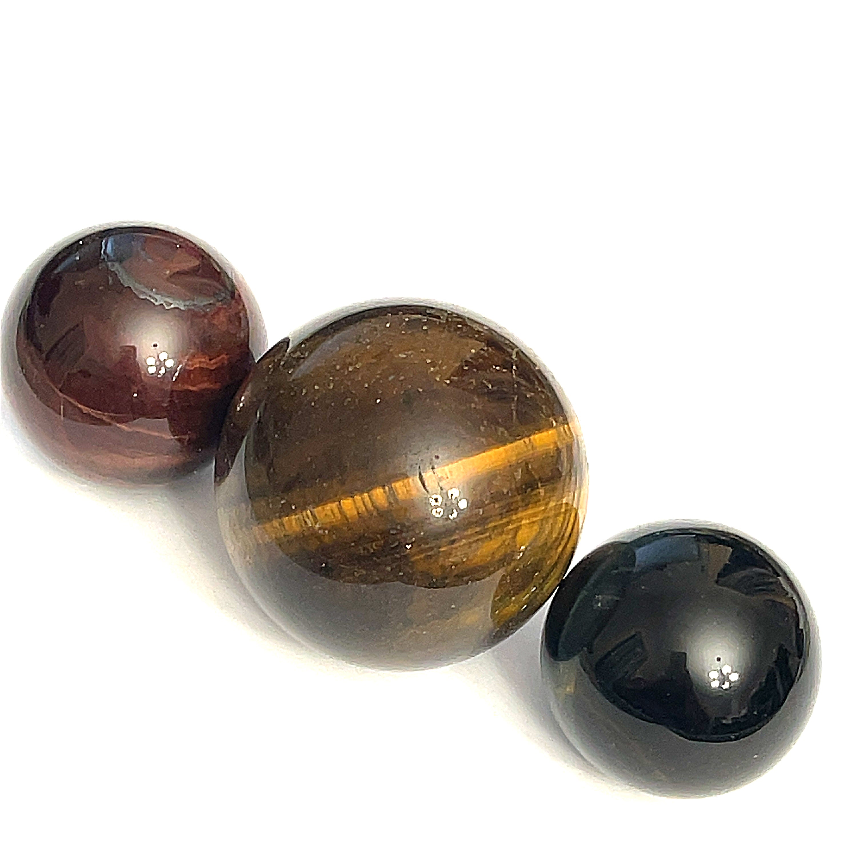 A collection of red, golden, and blue tiger eye gemstone spheres, displayed on a white background in a diagonal line, front view.