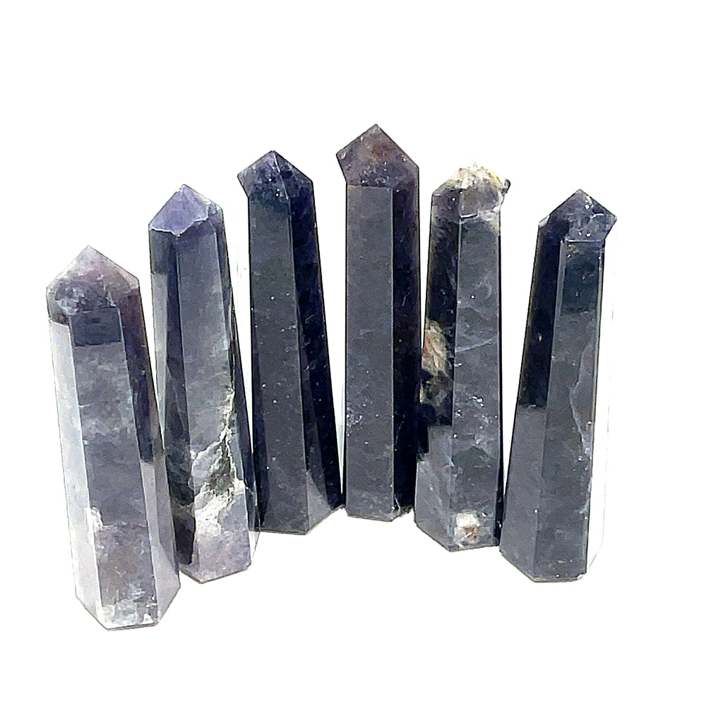 A collection of six Iolite gemstone towers displayed in a row, showing variations in color from light to deep blue with a purplish tint on a white background, front view. 