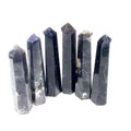 A collection of six Iolite gemstone towers displayed in a row, showing variations in color from light to deep blue with a purplish tint on a white background, front view. 