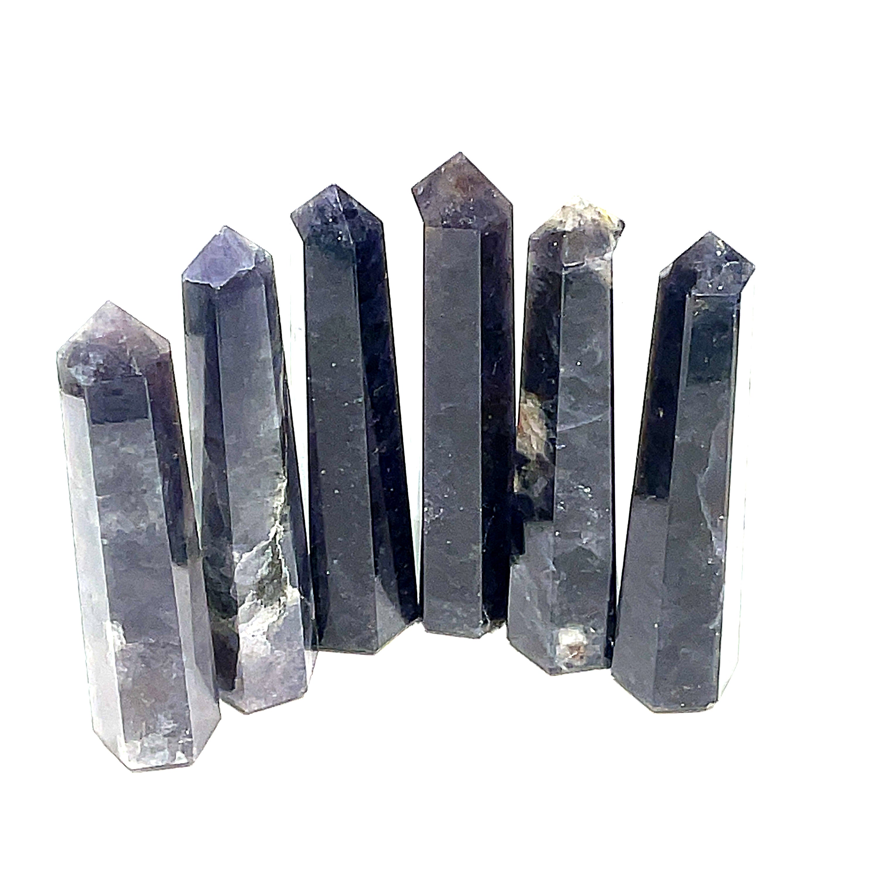 A collection of six Iolite gemstone towers displayed in a row, showing variations in color from light to deep blue with a purplish tint on a white background, front view. 