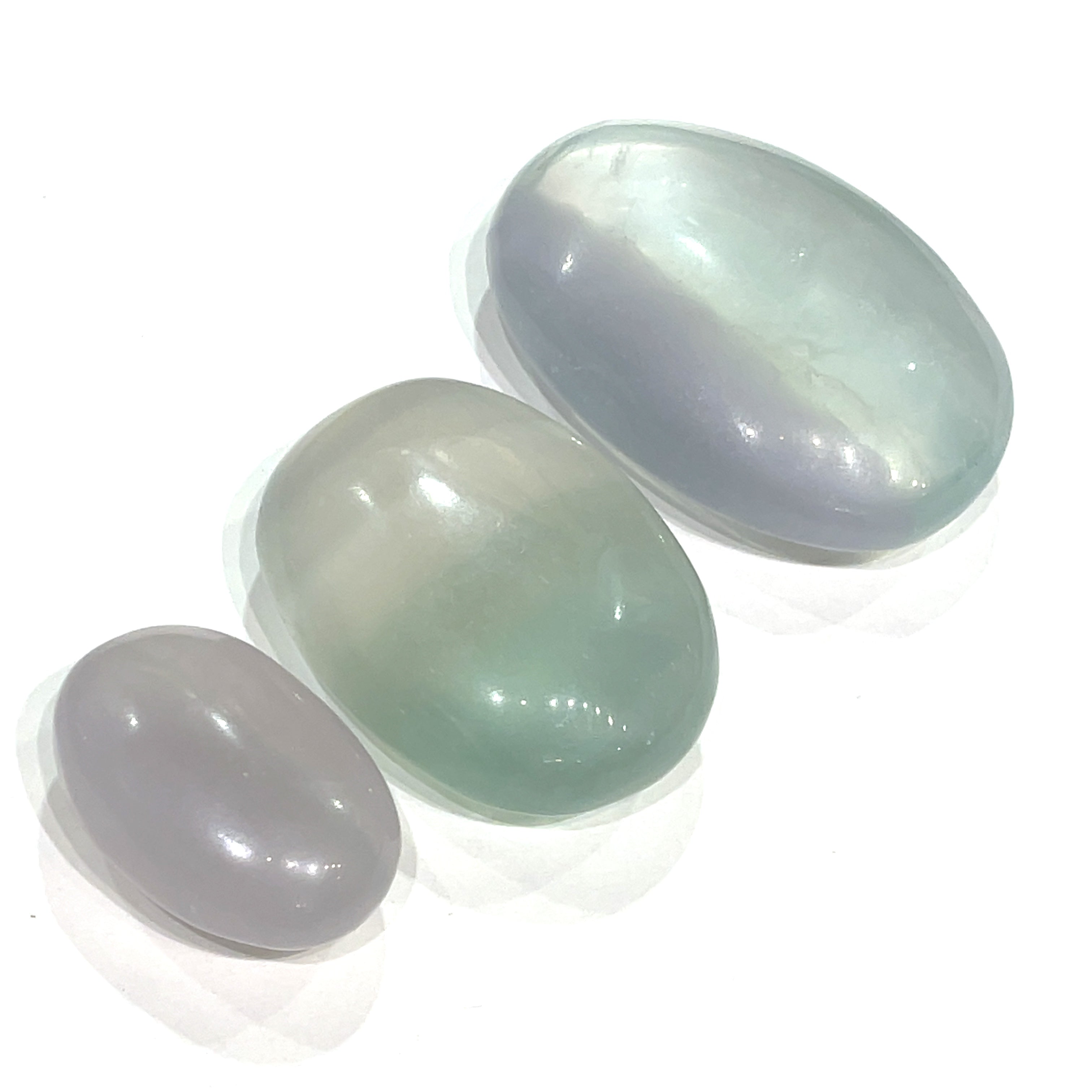 A collection of smooth, rounded gemstone palm stones displaying varying shades of lavender and green, with a milky translucency on a white background. 