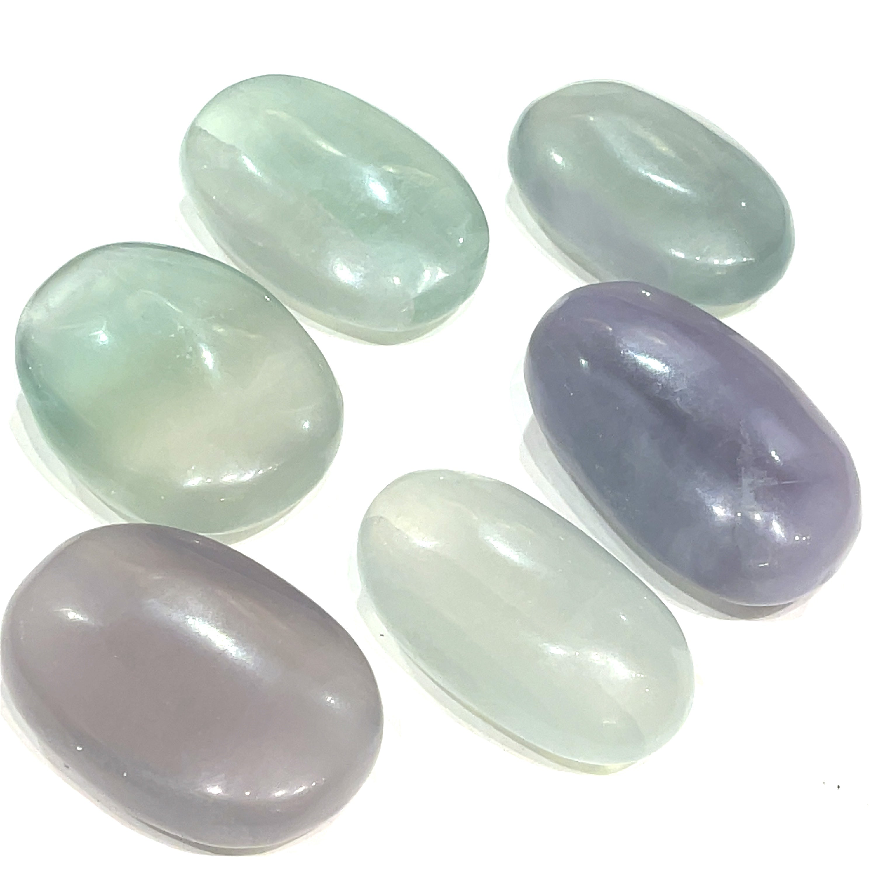 A collection of smooth, rounded gemstone palm stones displaying varying shades of lavender and green, with a milky translucency on a white background close up  overview.