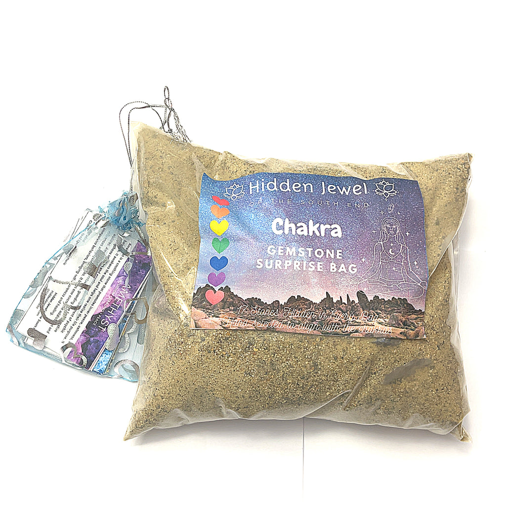 A collection of various raw gemstones in a bag of sand, each with a small information card indicating the type of gemstone. The gemstones are colorful and displayed against a white background in a front overview.