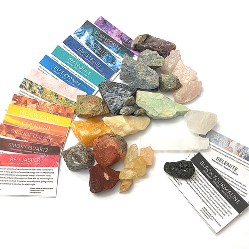 A collection of various raw gemstones is spread out, each with a small information card indicating the type of gemstone. The gemstones are colorful and displayed against a white background in a front overview.