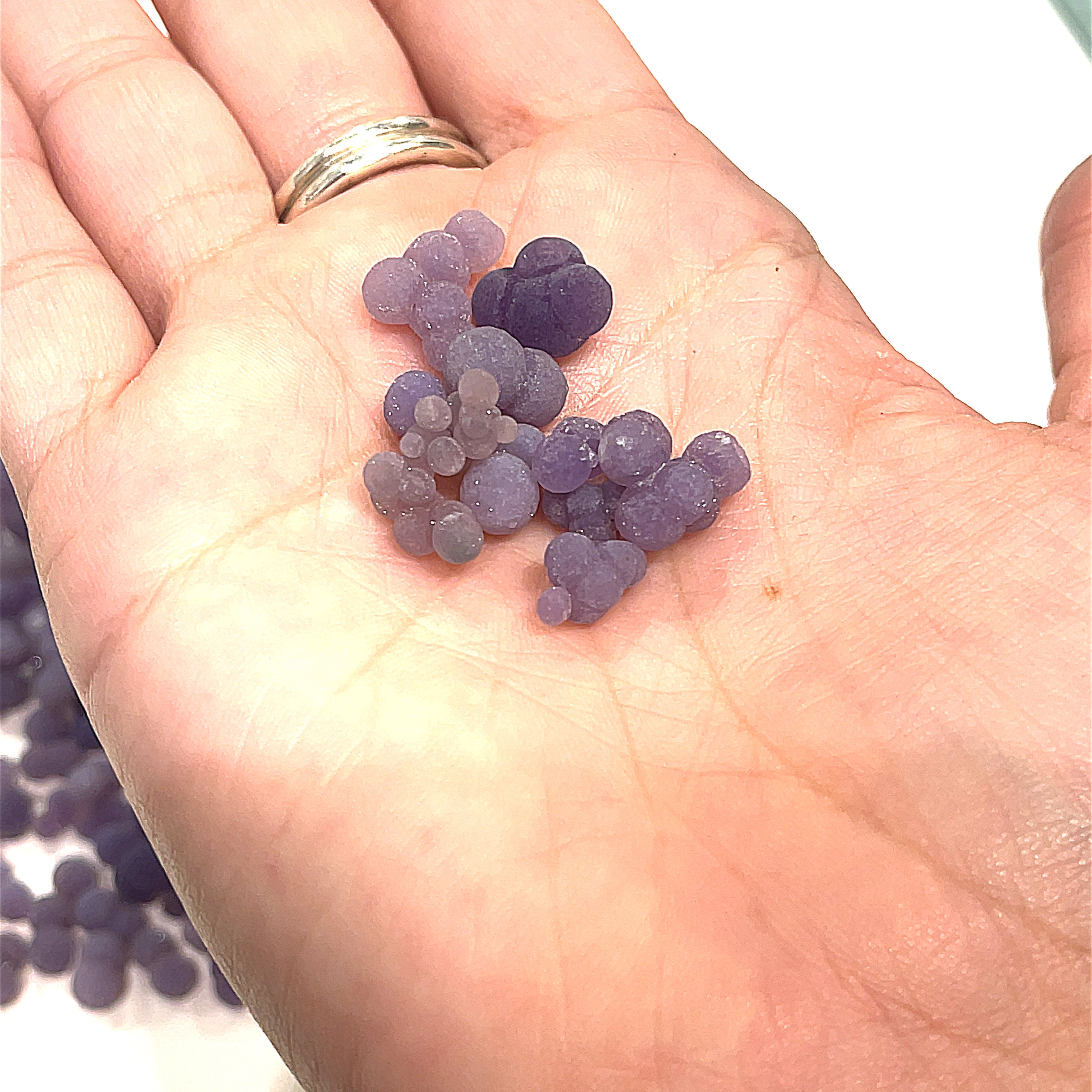 A collection of xs grape agate gemstone on a models hand on a white background, front close up overview. 