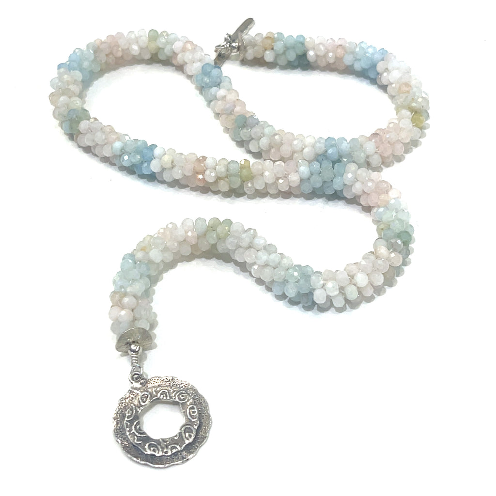 A crocheted morganite gemstone necklace with a variety of colorful beads and a sterling silver decorative toggle on a white background, a  center, long overview. 