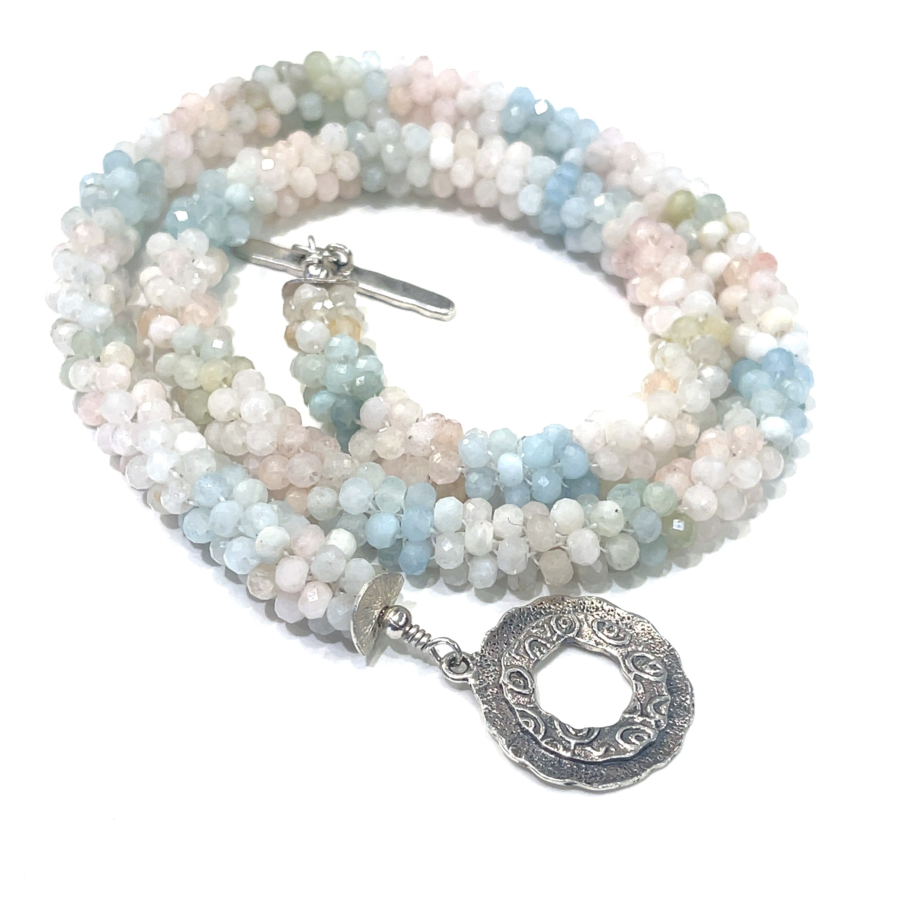A crocheted morganite gemstone necklace with a variety of colorful beads and a sterling silver decorative toggle on a white background, a  spiral center, close up overview. 