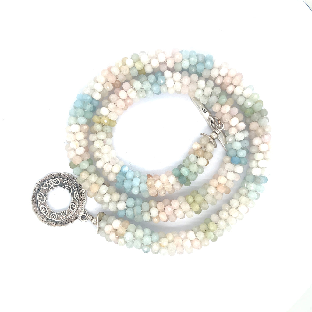 A crocheted morganite gemstone necklace with a variety of colorful beads and a sterling silver decorative toggle on a white background, a spiral center overview. 