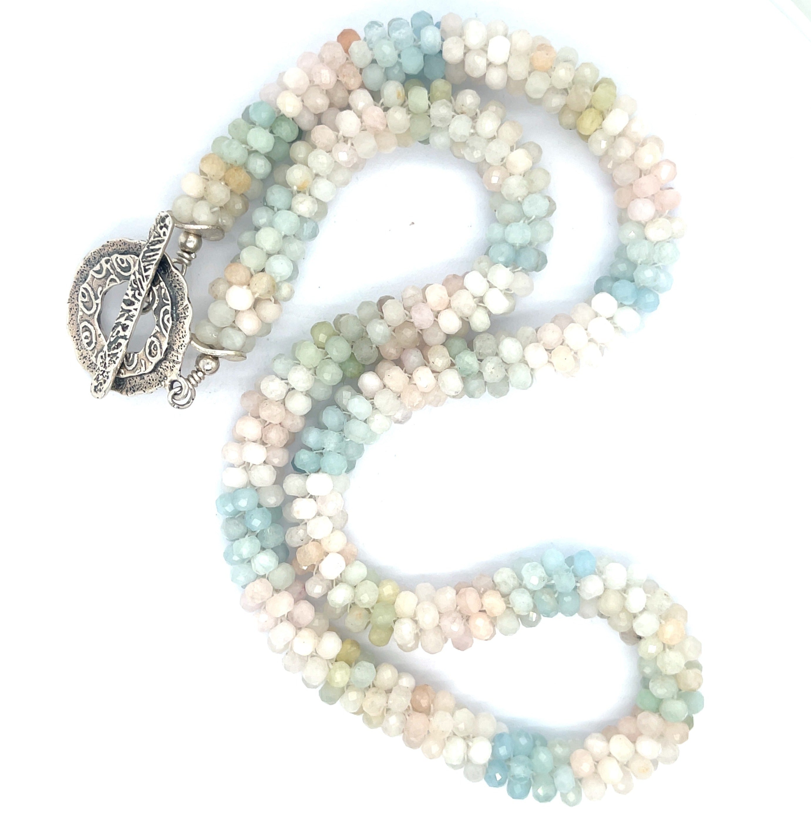 A crocheted morganite gemstone necklace with a variety of colorful beads and a sterling silver decorative toggle on a white background, center overview. 