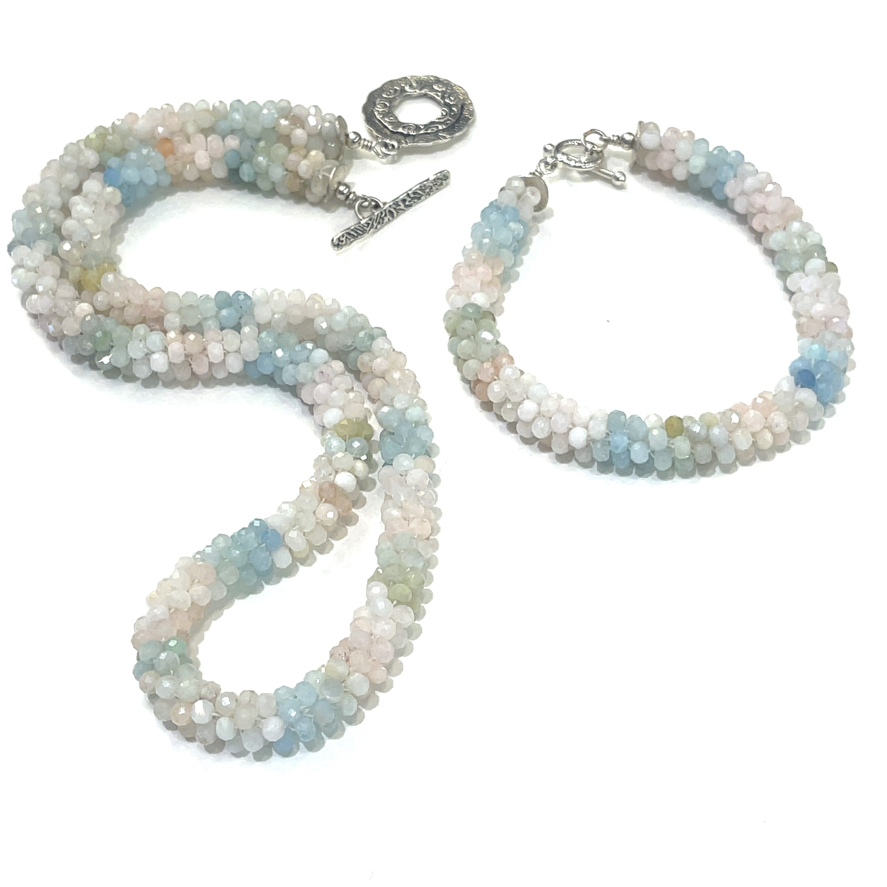 A crocheted morganite gemstone necklace with its matching bracelet with a variety of colorful beads and a sterling silver decorative toggle on a white background, a  center overview. 