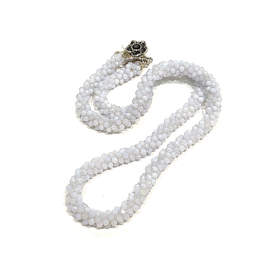 A crocheted necklace made with blue chalcedony gemstones, featuring a sterling silver flower box clasp and a black gemstone detail on a white background, long, front, close up overview.