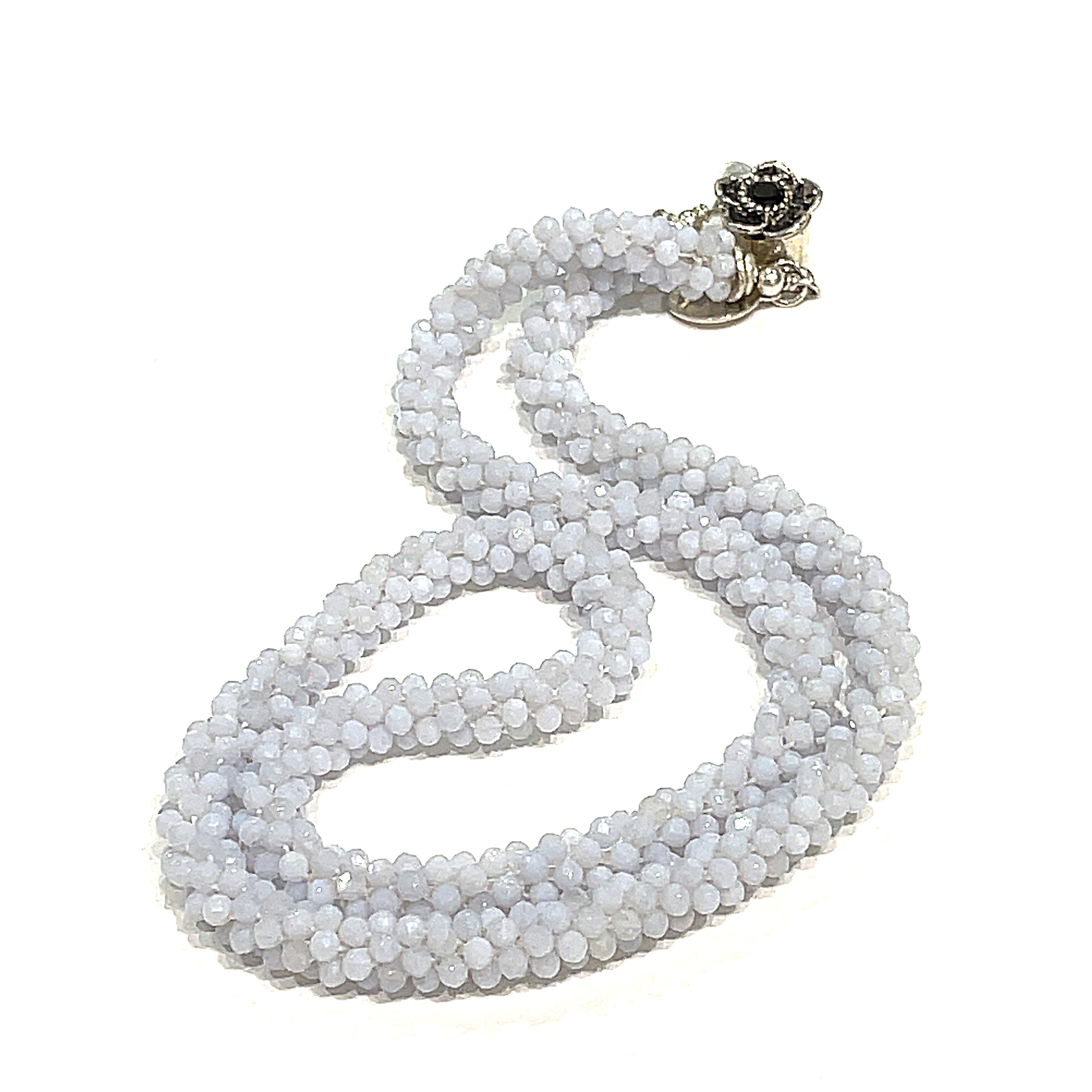 A crocheted necklace made with blue chalcedony gemstones, featuring a sterling silver flower box clasp and a black gemstone detail on a white background, long, front overview. 
