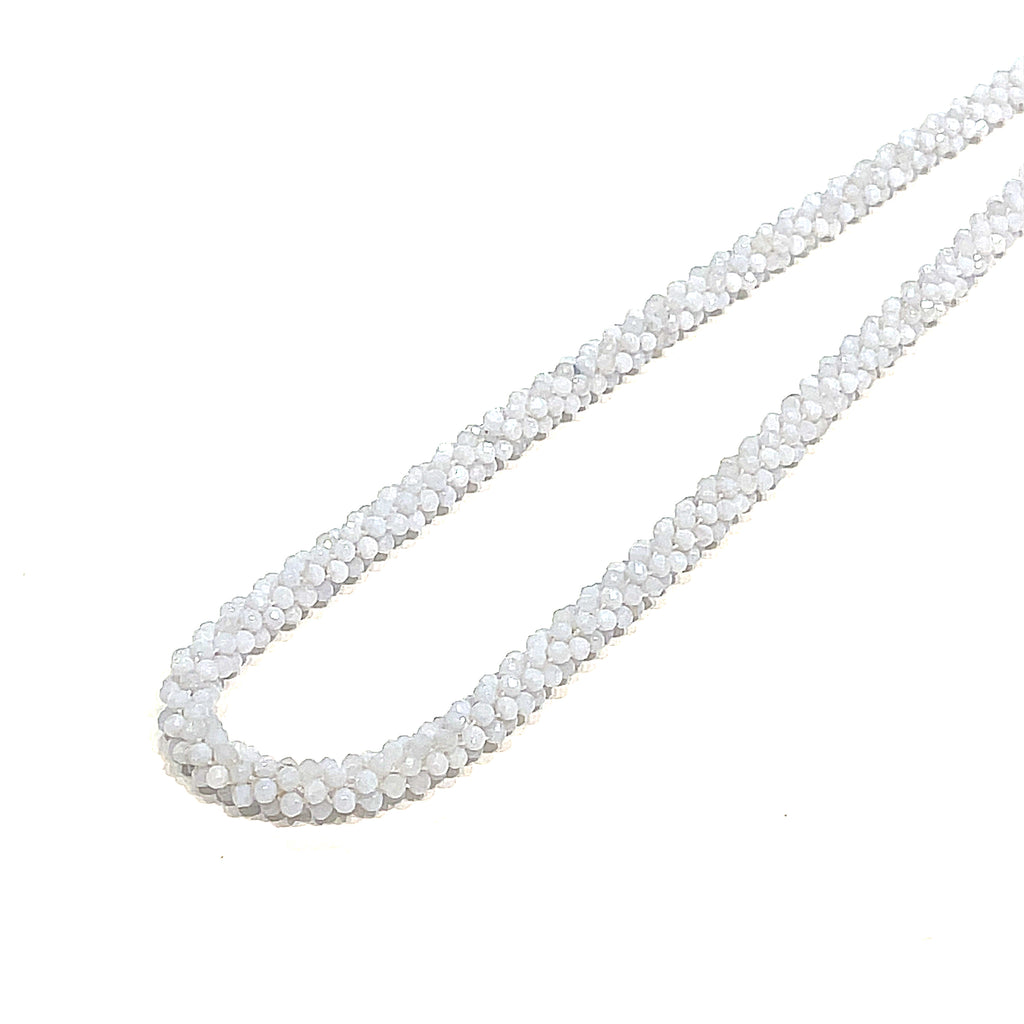 A crocheted necklace made with blue chalcedony gemstones on a white background, long, diagnola left angle front overview.