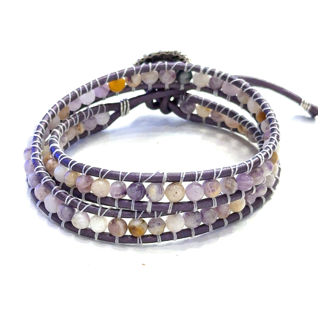 A double leather wrap bracelet made out of purple flower agate, featuring a floral button, and measuring 15.5 inches in length. On a white background button front view.