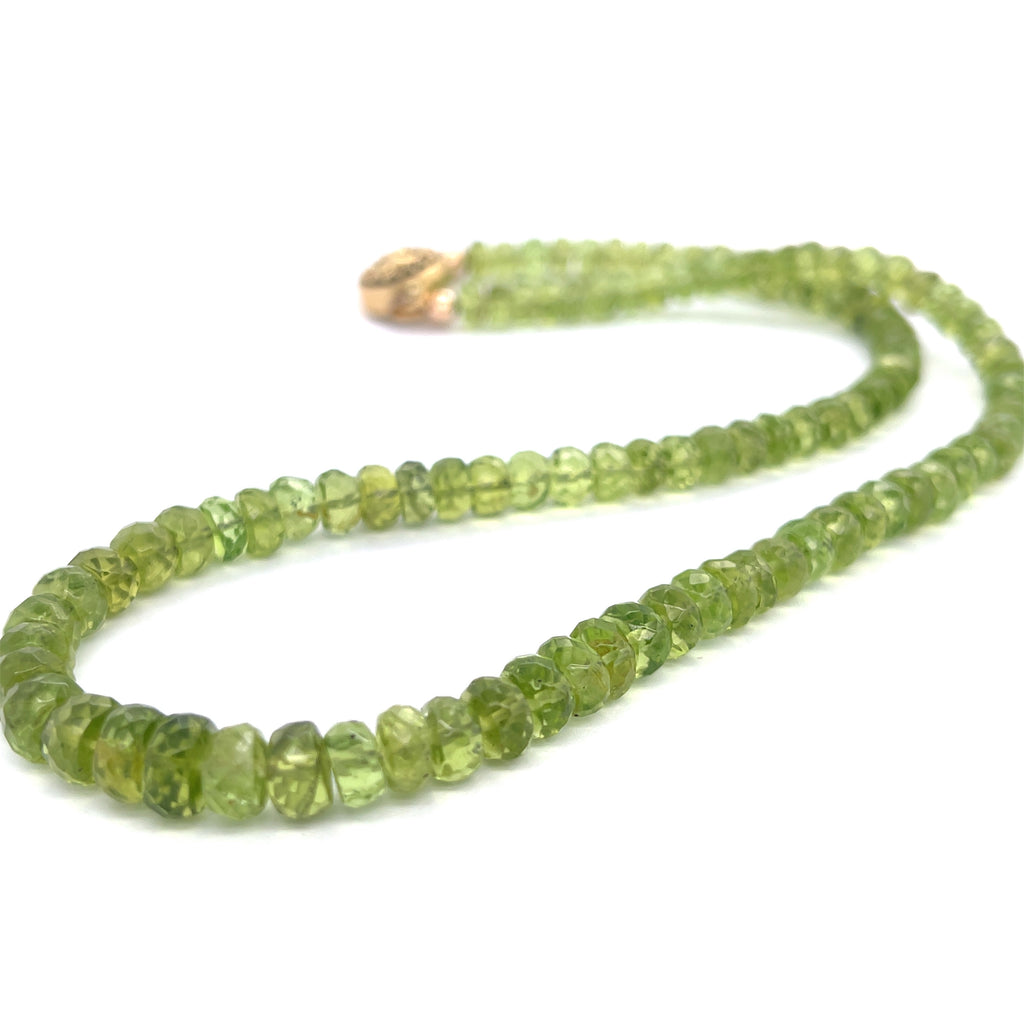 A green beaded peridot gemstone necklace with gold-filled findings and a sun and moon box clasp on a white background, long angled flat overview.