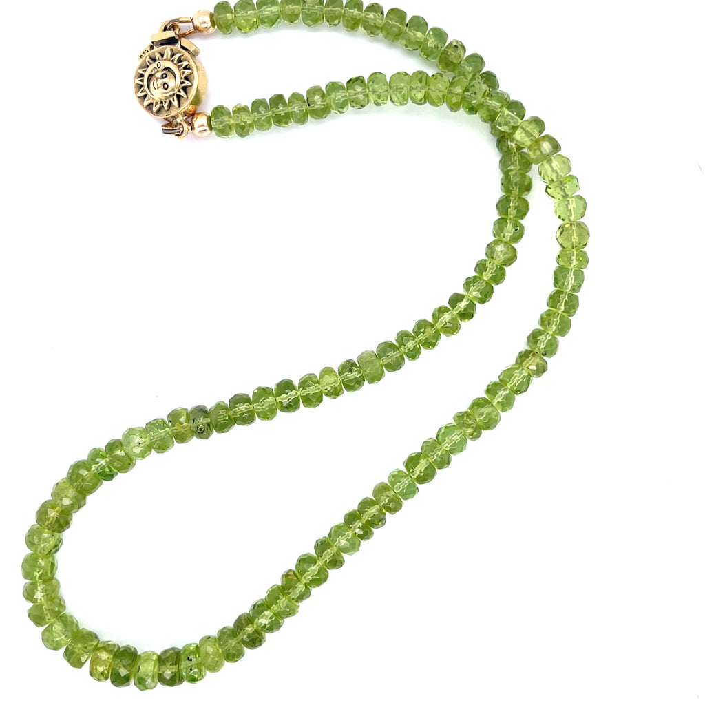 A green beaded peridot gemstone necklace with gold-filled findings and a sun and moon box clasp on a white background, long overview.