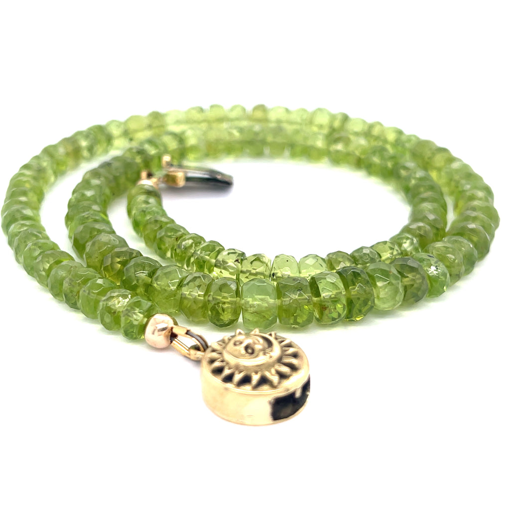 A green beaded peridot gemstone necklace with gold-filled findings and a sun and moon box clasp on a white background, spiral flat overview.