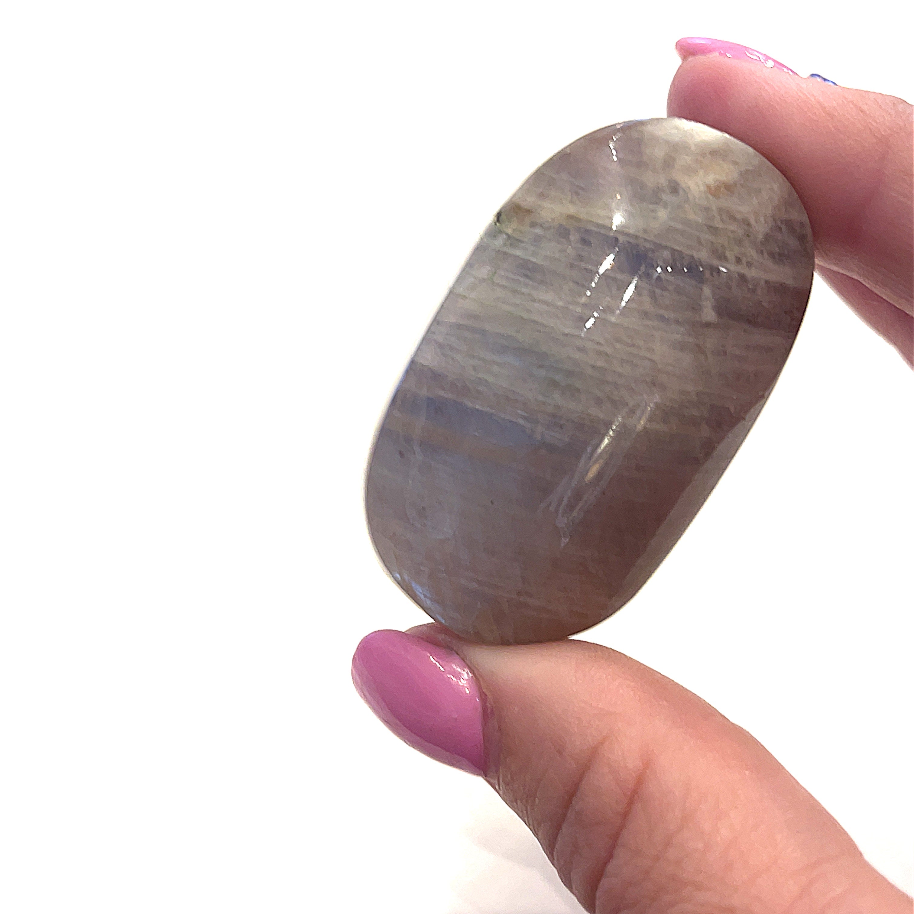 A grey moonstone palm stones displayed in a models finger tips on a white background front overview.