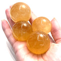 A group of Honey Calcite Sphere – ethically sourced golden crystal for clarity and confidence in a models hand for a close up view. 