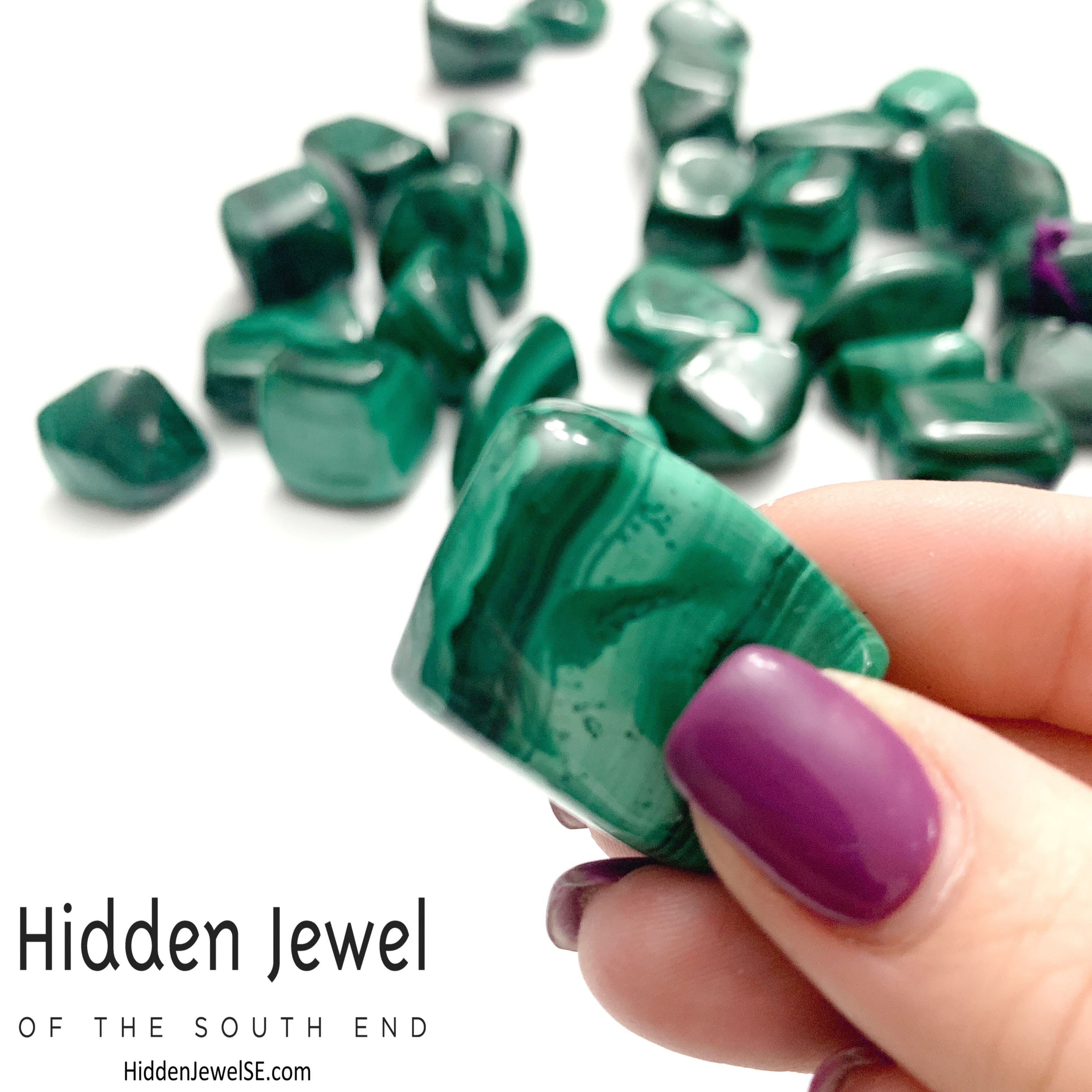A group of Malachite tumbled  gemstone  on a white background, and one in a models finger tips, front view.