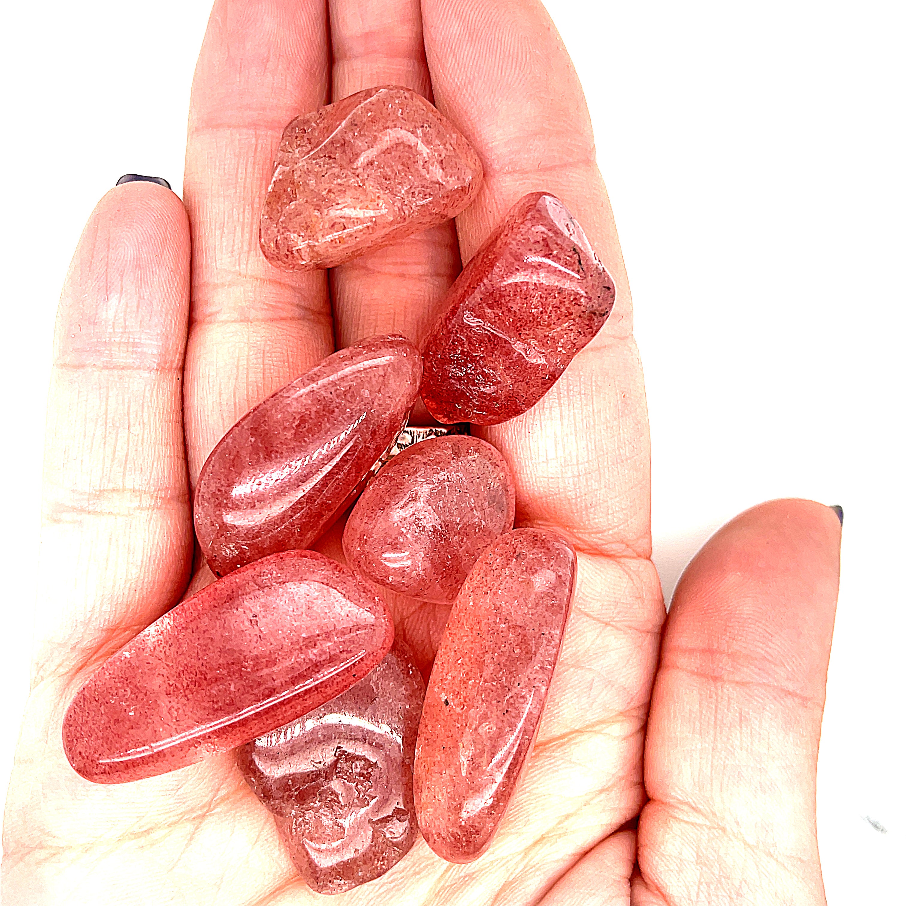 A group of Strawberry Quartz tumble gemstone in a models palm on a white background, front view.