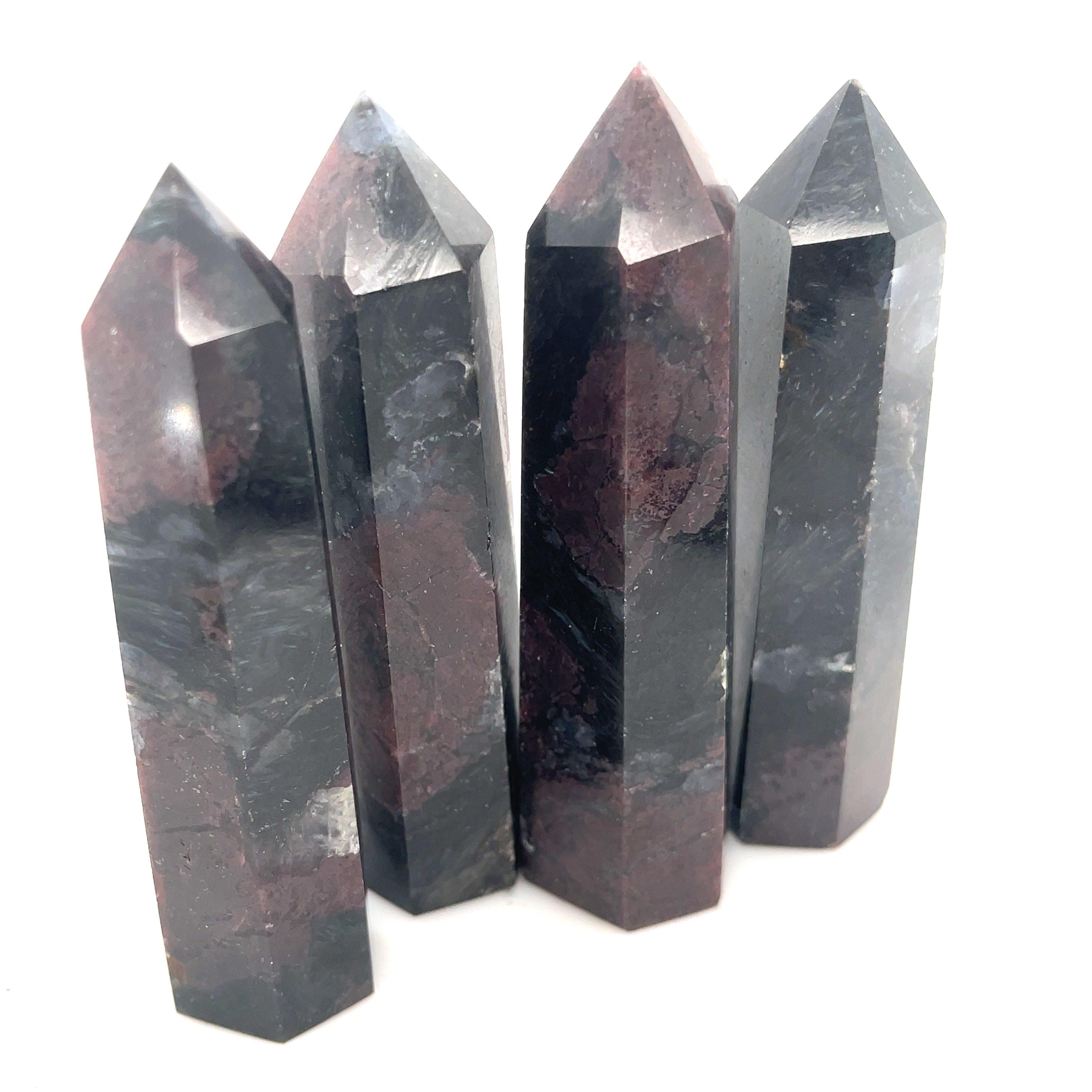 A group of  four dark colored gemstone towers arranged in a row, with a variation in size and shape, representing the Garnet and Astrophyllite gemstones on a white background overview. 